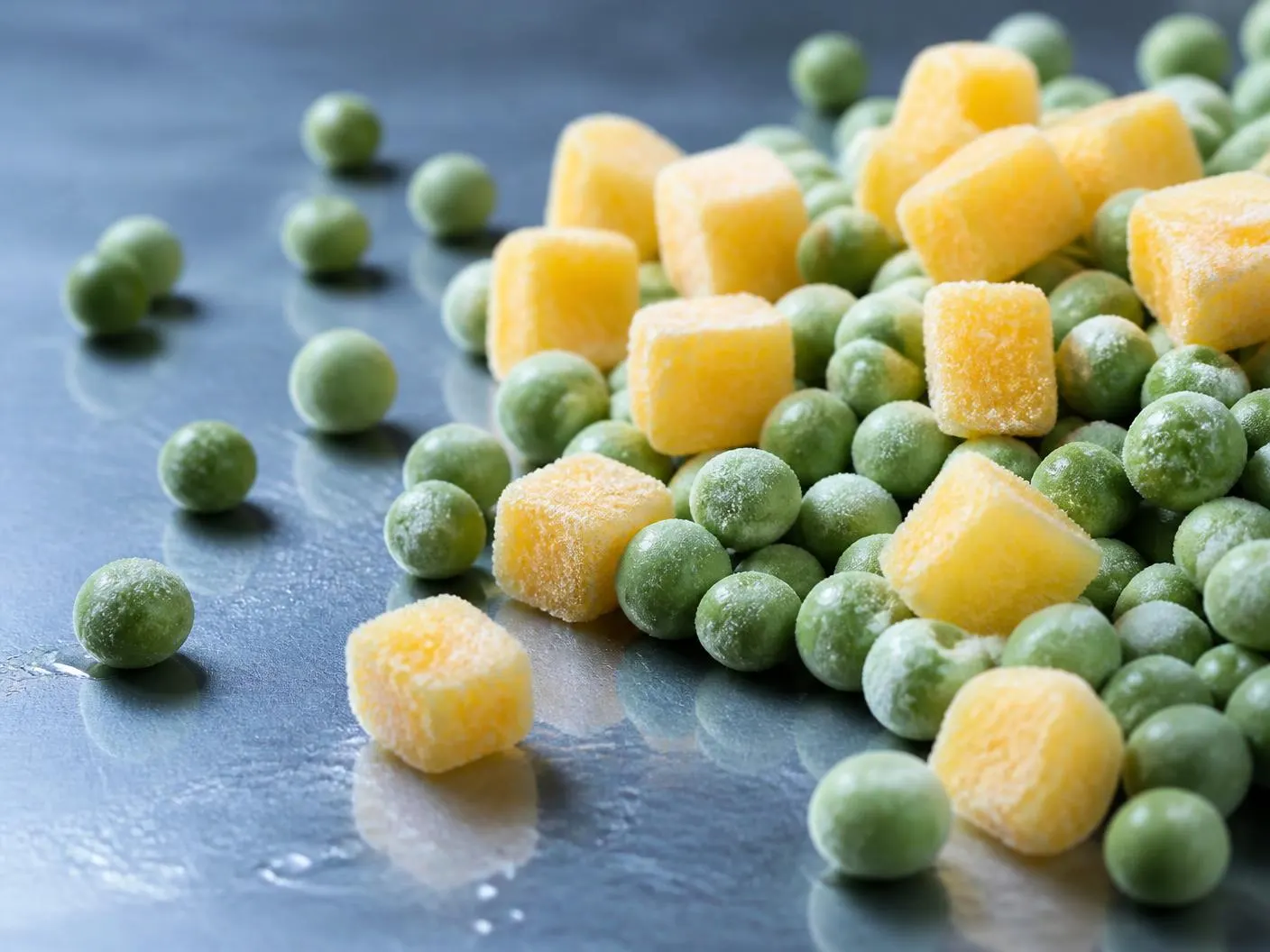 Individually quick frozen mango cubes and green peas with frost crystals on a cold steel surface