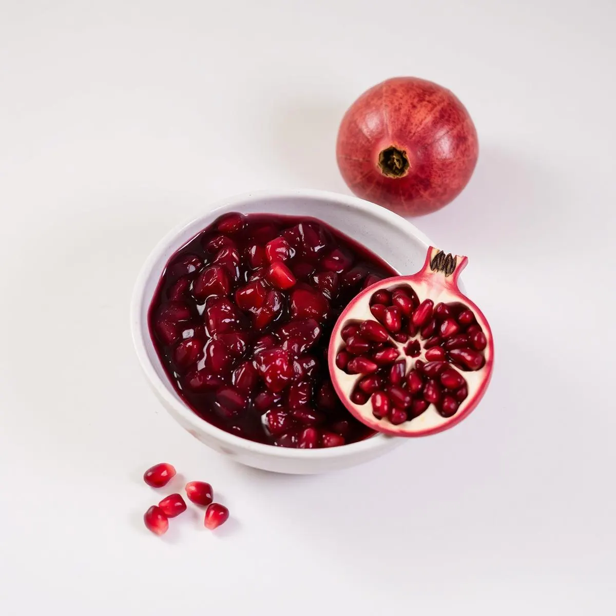 Deep red pomegranate pulp in a ceramic bowl beside a halved pomegranate
