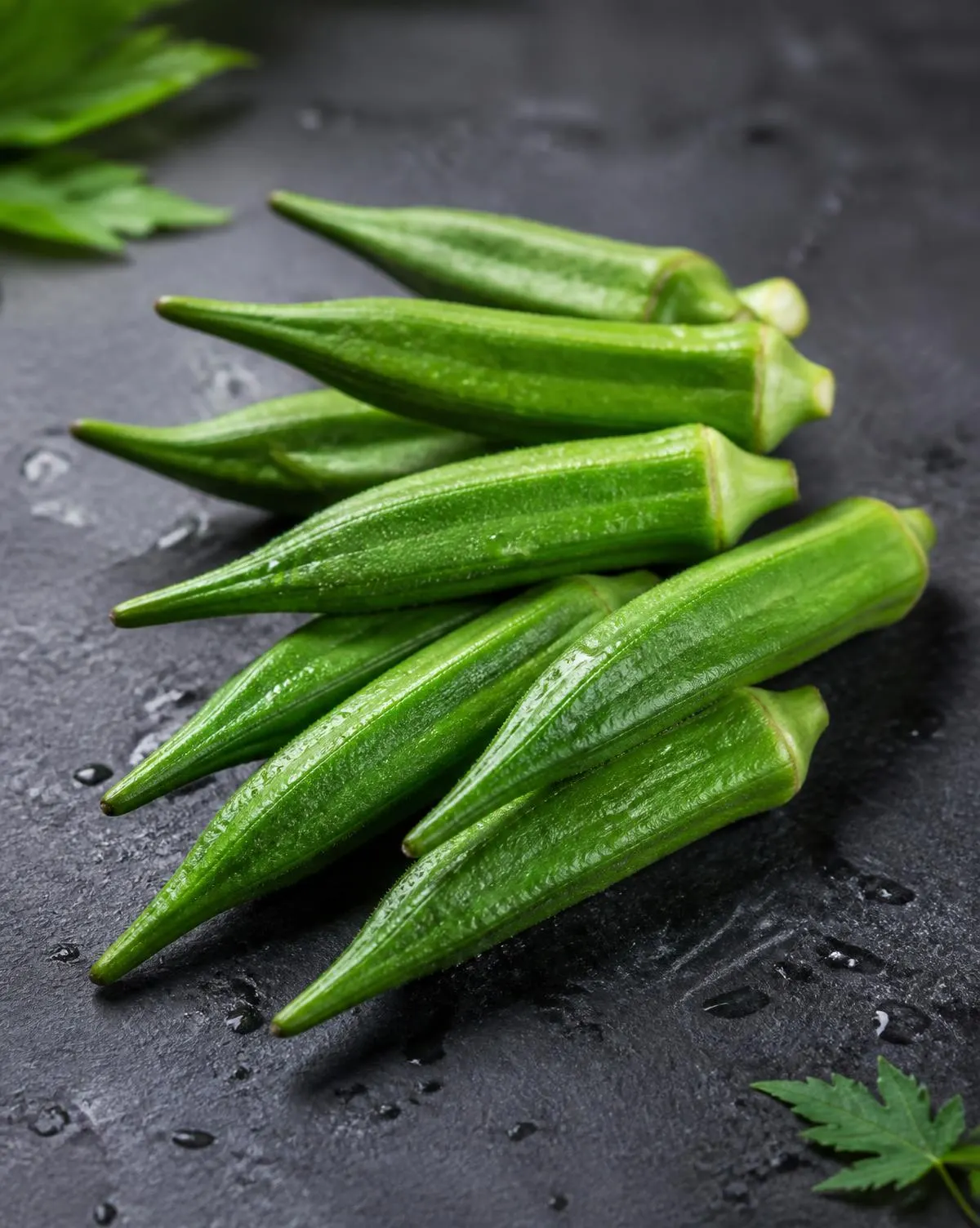 Fresh green okra pods on a dark slate surface